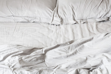 View of an unmade bed with crumpled bed sheet, a blanket and two pillows. Selective focus