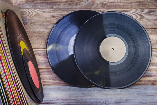 A Pile Of Old Vinyl Records Stand On A Shelf Against The Background Of A Wooden Wall