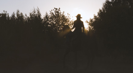 Silhouette of a woman in cowboy hat riding a horse - sunset