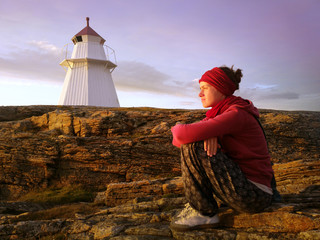 junge Frau sitzt bei Abendsonne am Leuchtturm und genießt die Einsamkeit
