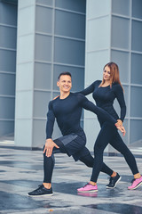 Fototapeta na wymiar Fitness couple is stretching over modern building background.