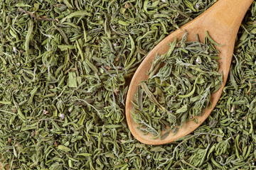 Extreme close up of an organic, dried savory spice and a wooden spoon. Herbal food macro backgrond
