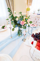 Table set for wedding banquet with floral composition of roses. Flower decoration in tall vase.
