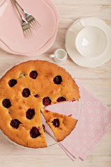 Homemade plum cake on a glass stand and pink plates.
