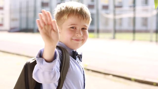 A smiling schoolboy waving good-bye and running to school. 
