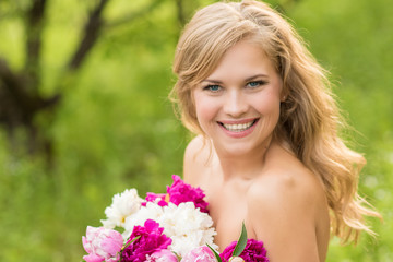 Naklejka premium Beautiful smiling woman with a wreath of peonies on the head, holding a bouquet in the nature