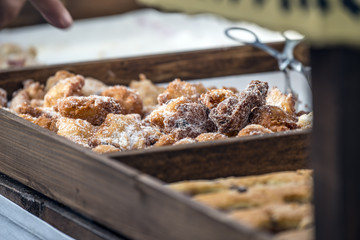 Frittelle con granella di zucchero, mentre un dito indica la scelta nell'espositore in legno