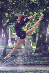 Fototapeta na wymiar Beautiful ballerina girl in casual clothes posing on a blurred background of the park trees on background feet closeup