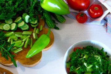 salad from pepper, parsley, tomato and cucumber in a white bowl on white wooden table