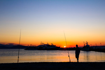 Silhouetted shot of a senior man fishing on pier at sunset