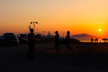 Silhouetted shot of young people are having fun on beach and playing football