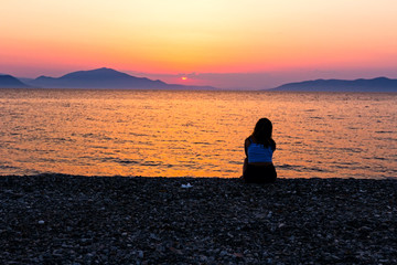 Silhouetted shot of young woman alone by the beach in silence looking on the water