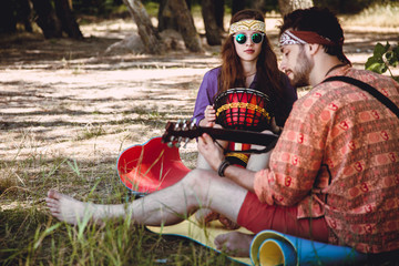 Beautiful young couple in love in hippie style rest on the nature. A man plays the guitar and the girl plays the drum