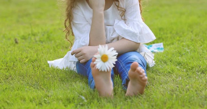 Happy girl with daisy in her bare foots, at green grass in a summer park.