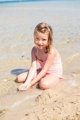 Pretty little girl playing with sand on the beach. Summer time