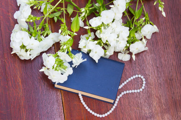 Book with white flowers and pearl necklace on wooden background.