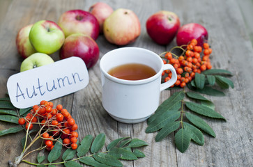 Cup of tea and autumn harvest of apples on a wooden table, yellow leaves concept of autumn, mood and coziness.