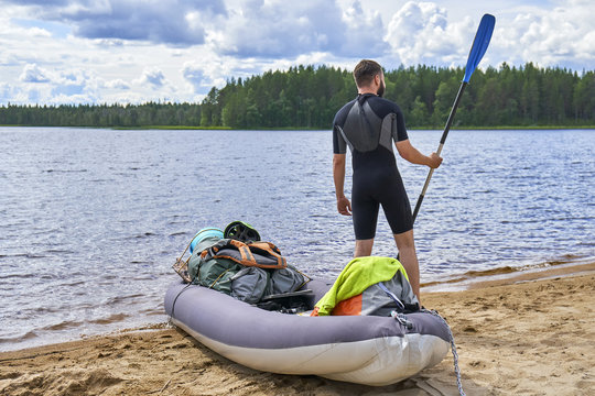  Young man standing on the lake shore holding a paddle ready to sail on the inflatable kayak