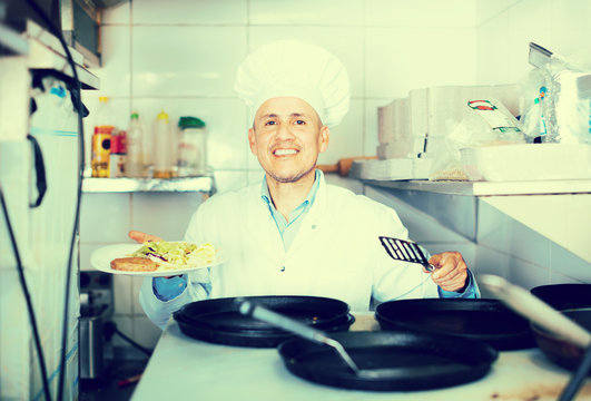 Smiling professional cook sitting on kitchen