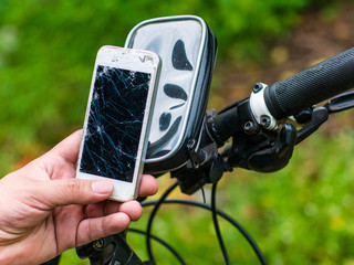 Man's hand holding a broken mobile phone with bicycle and nature background