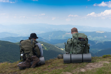 Two tourists sitting on a cliff against a background of mountains