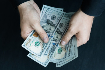 The white young man counts the money, one hundred new dollar bills on a black background close plan. Concepts of business and finance. top view .