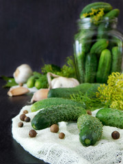 Cucumbers and ingredients for conservation are scattered on a dark table