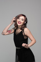 Smiling young woman with tattoos listening to music in big headphones