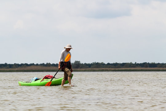 Girl walks in shallow water and pulls a green kayak. Kayaking in wild Danube river on biosphere reserve in spring