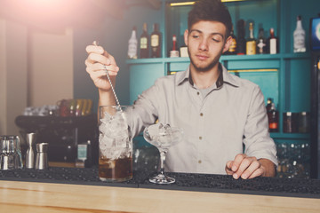 Young bartender mixing cosmopolitan cocktail