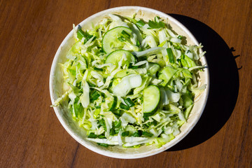 Spring vegan salad with cabbage, cucumber, green onion and parsley on wooden table