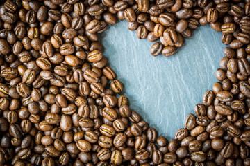 Pea berry coffee beans with heart shape on stone plate , top view and copy space