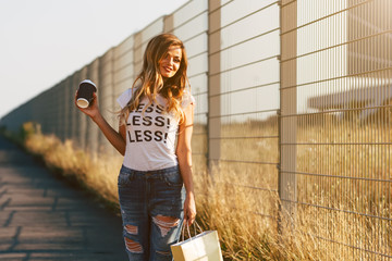 Beautiful woman walking with coffee and shopping bag in white T-shirt with word "less"