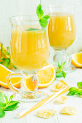 Orange juice in a glass on a white wooden table with whole and sliced ​​oranges