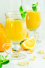 Orange juice in a glass on a white wooden table with whole and sliced ​​oranges