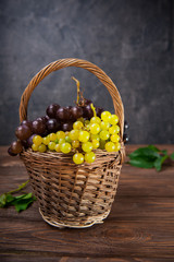 Wicker basket with various grapes: red, white and black berries on the dark wooden table. Selective focus. Copy space