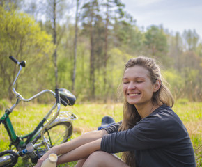 Obraz premium Smiling blond woman resting while sitting on the lawn while walking on a bike