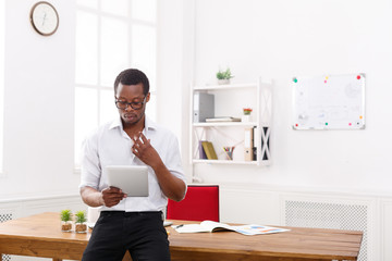 Concentrated black businessman in modern office, work with tablet