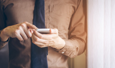 Businessman standing near window and using cell phone vintage tone.