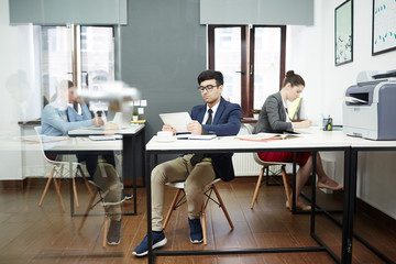 Busy modern open plan office: talented young designers sitting at desks and working on promising project, room illuminated with daylight