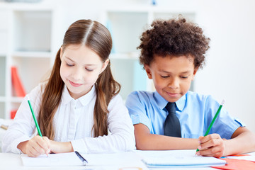 Two little classmates of elementary school drawing in copybooks