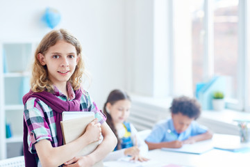 Elementary youngster with copybooks and his classmates on background