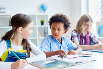 Clever schoolkids discussing something in textbook during lesson of literature