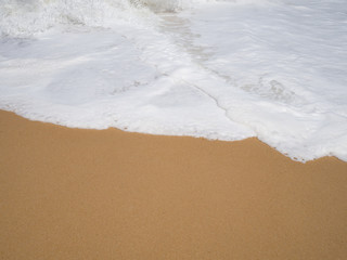 White soft sea foam wave layer with brown sand on beach in sunny day for background.