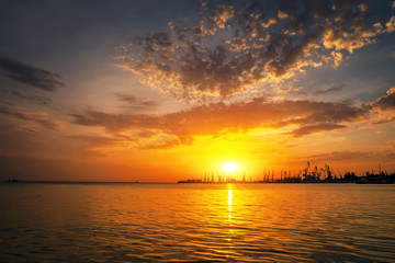 Cranes silhouettes against fiery, orange and red sky. Beautiful Azov Sea at sunrise. Harbor of Berdyansk during sunset.