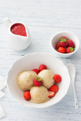 Vegan banana ice cream with strawberry sauce and fresh strawberries in a white bowl on a light blue wooden background