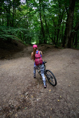 young girl in sport wear with bicycle riding in forest in summer