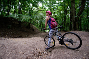 young girl in sport wear with bicycle riding in forest in summer