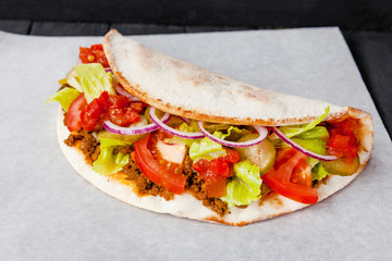 Street food calzone, stromboli wrapped in paper on a black background