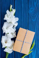 Preparing to celebration. Box in kraft paper near flower gladiolus on blue wooden table top view copyspace